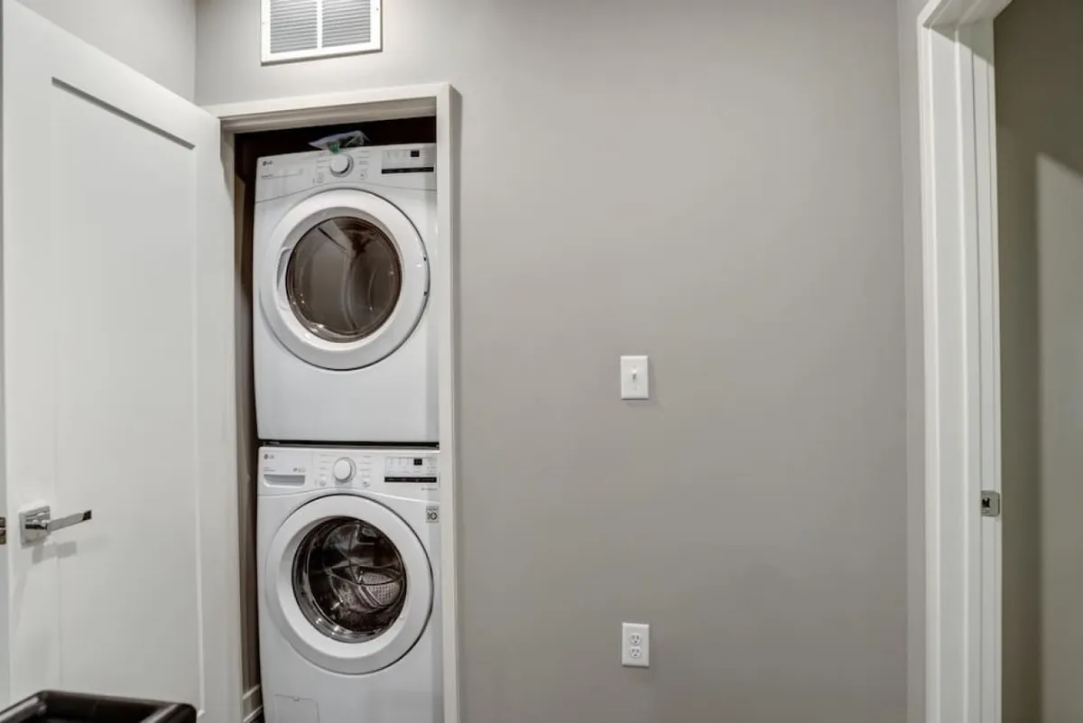 Compact and practical laundry facilities with a stacked washer and dryer, minimalist cabinetry, and neutral wall colors. The organized space is functional for handling everyday laundry needs during longer stays or family visits.