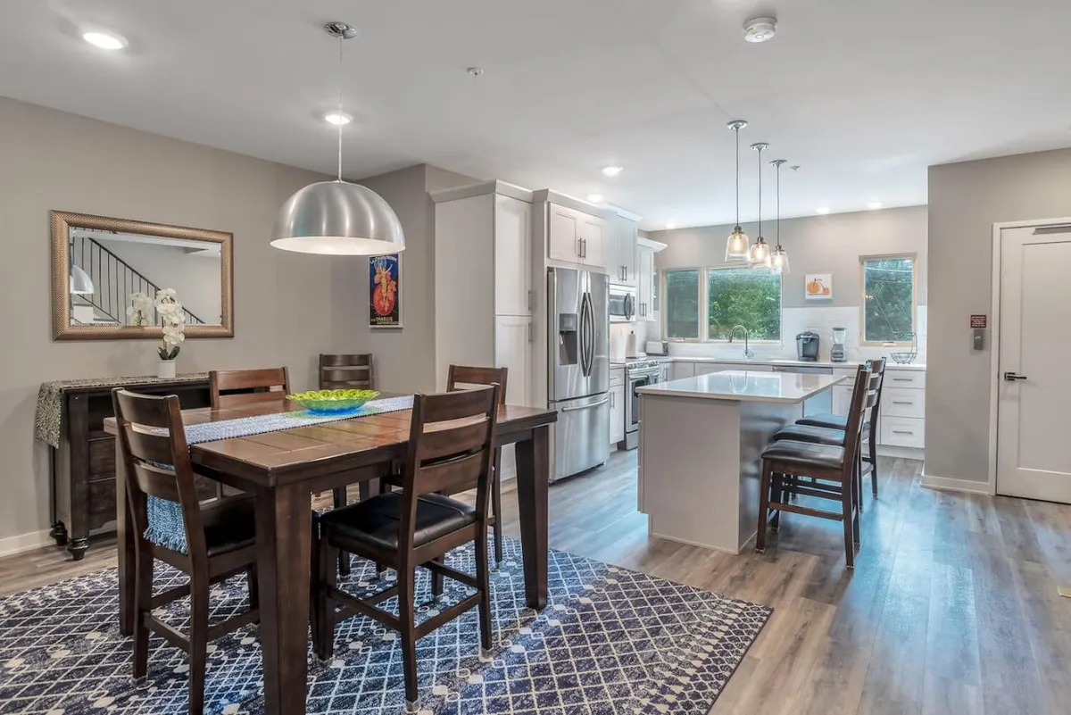 This image shows an expansive open-concept dining and kitchen area, including a central island, contemporary light fixtures, and modern appliances, set for both cooking and entertaining guests.