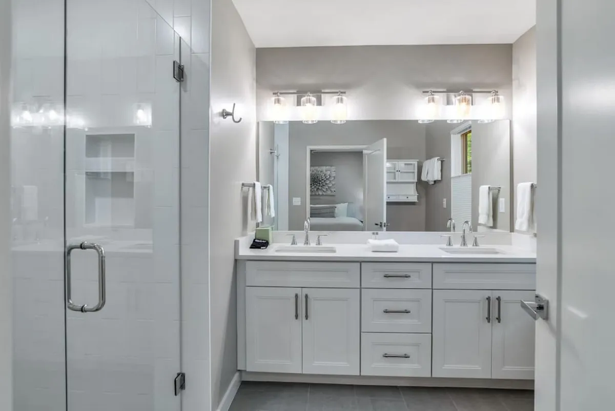 A modern bathroom with a double sink vanity, glass-enclosed shower, and stylish lighting fixtures. The clean lines and calming atmosphere evoke a spa-like sense of relaxation, perfect for self-care routines after a busy day.