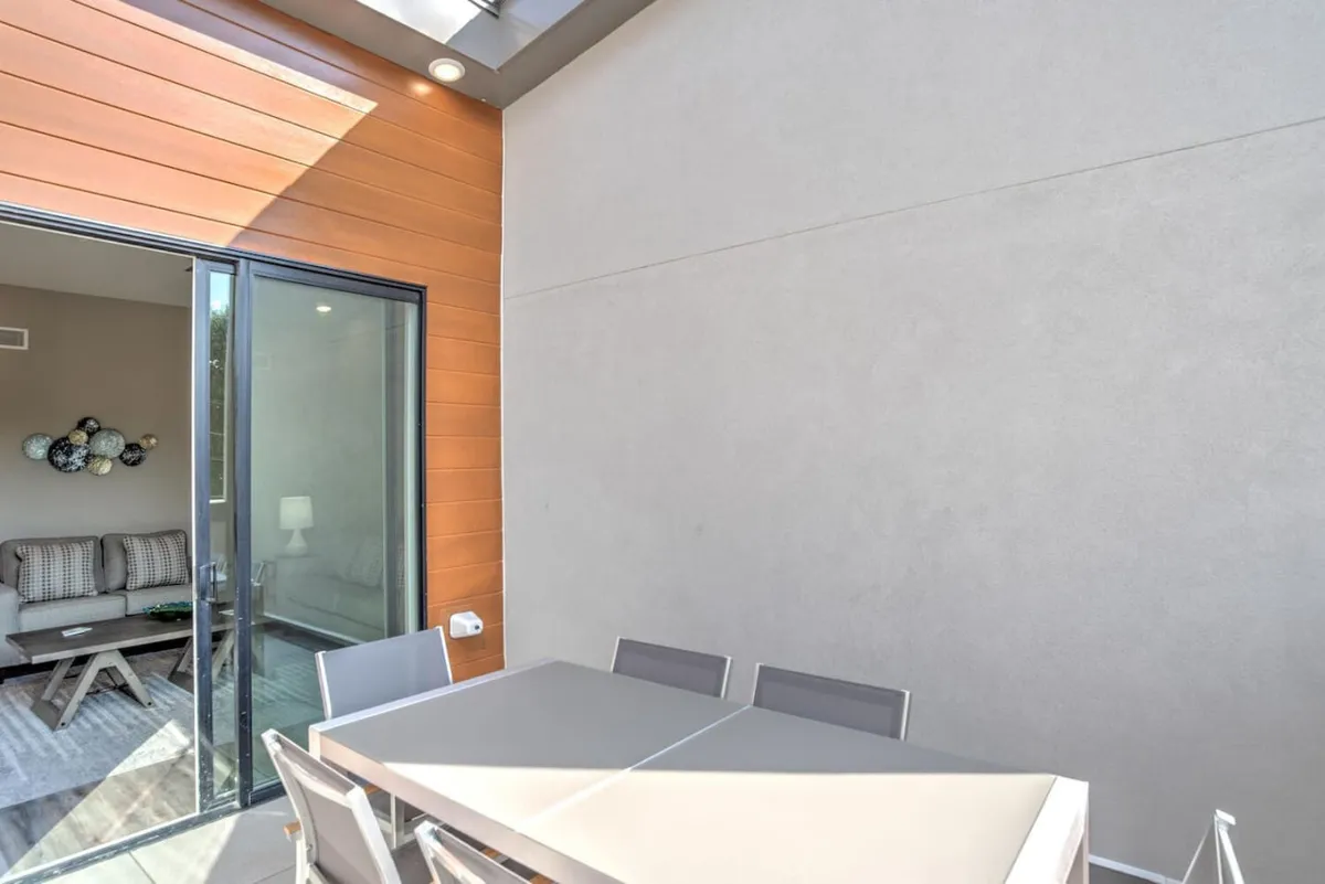 This exterior image features a stylish outdoor dining table set on a deck, with a sliding glass door offering a glimpse into the adjacent indoor seating area. The setting is casual yet elegant, ideal for sunset dinners, morning coffee, or relaxing outdoors while enjoying city views.