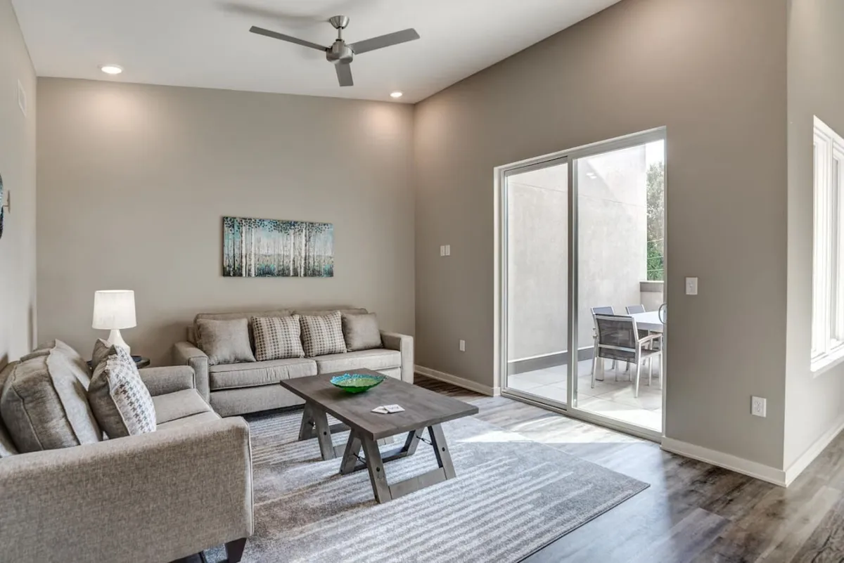This image captures a bright, cozy sitting area with a sofa and coffee table, complemented by artwork on the wall and a sliding glass door that opens to ample natural light. The space feels inviting, perfect for relaxing, reading, or enjoying casual moments with friends, reflecting the casual luxury of the top-floor retreat described in the section.