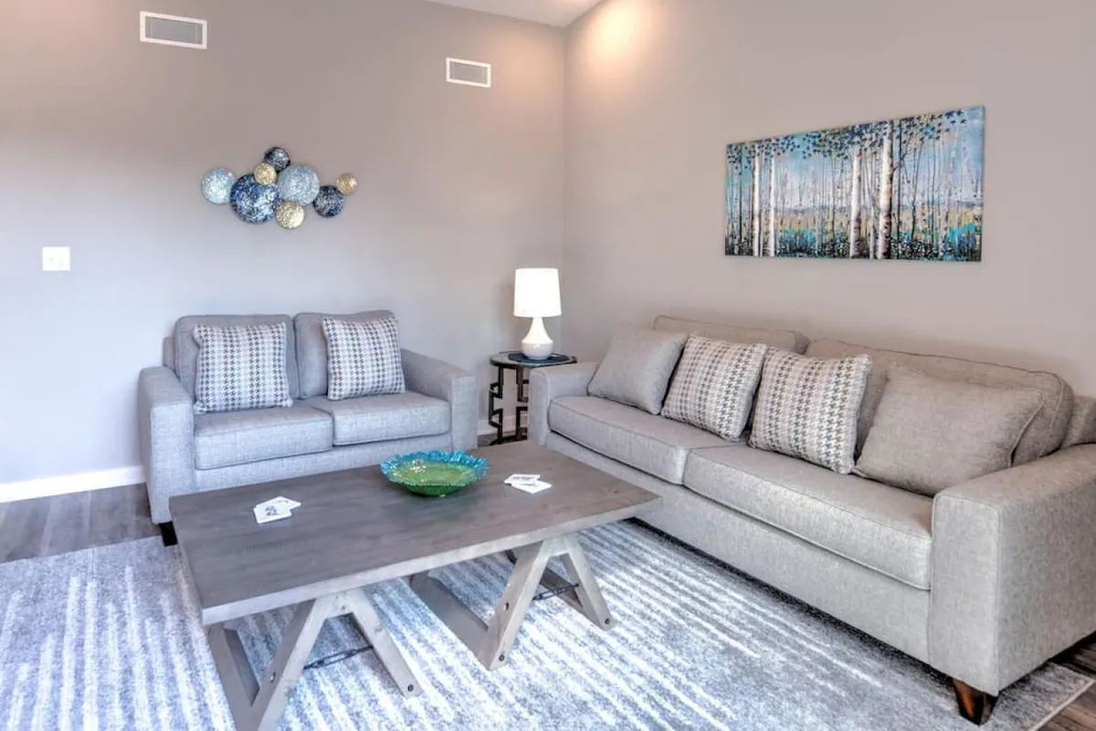 A cozy living space with two sofas arranged for easy conversation, a central coffee table, wall art, and a soft lamp. Ample daylight streams in, creating an uplifting mood that is conducive to both meetings and casual downtime.