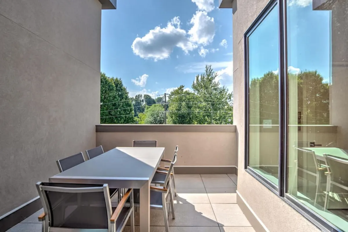 This image shows an outdoor dining table surrounded by greenery and expansive sky views, capturing the tranquility and openness of the deck. The mood is serene, emphasizing leisurely moments spent outdoors enjoying the scenery and fresh air above the city.