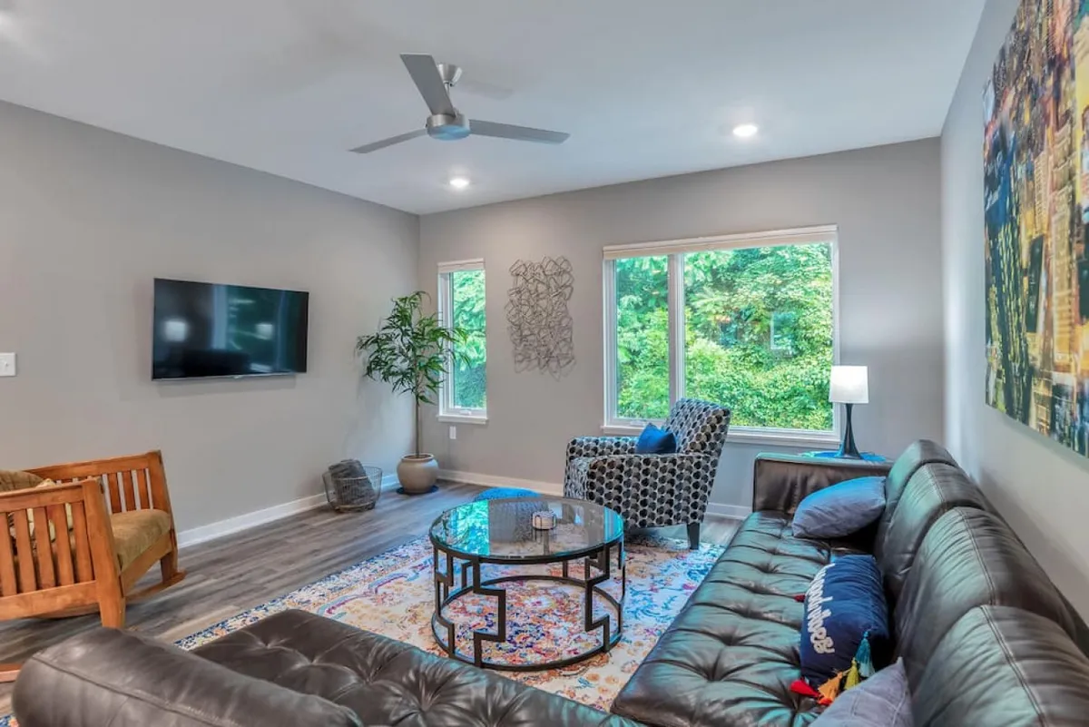 A welcoming living area featuring a leather sofa, decorative rug, coffee table, and large windows that let in plenty of natural light. The arrangement invites relaxation, socializing, and family downtime.